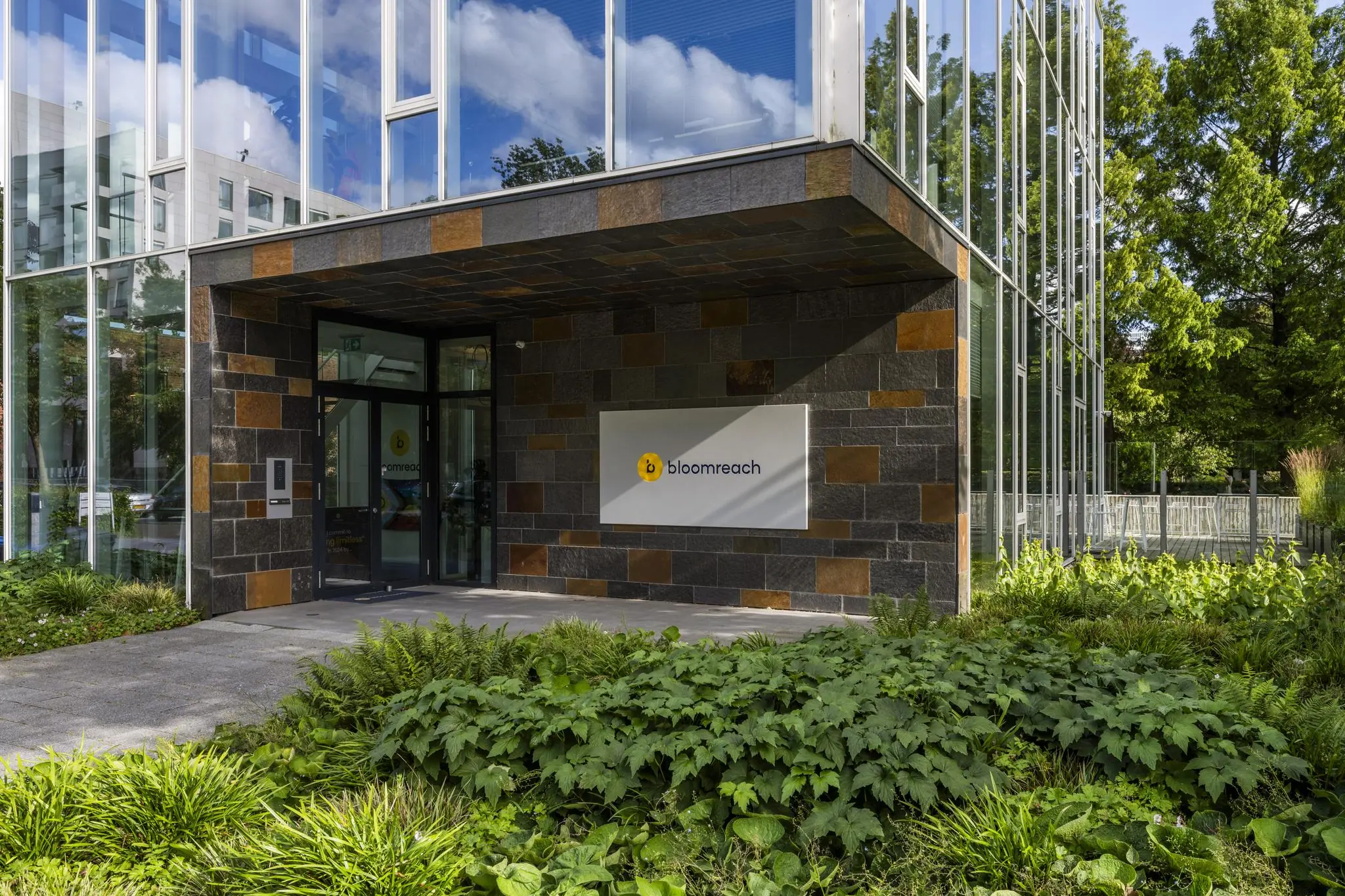 Entree van het kantoorgebouw van Bloomreach aan de Fred. Roeskestraat, met moderne gevel en omliggende beplanting.